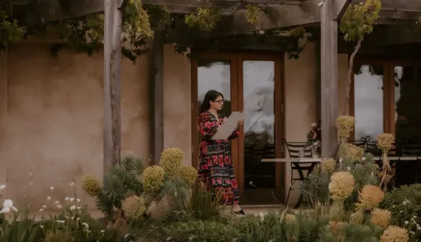 Artist Alyssa Bermudez sketching on a drawing board under a vine-covered pergola at a wedding, by Alyssa Bermudez Art