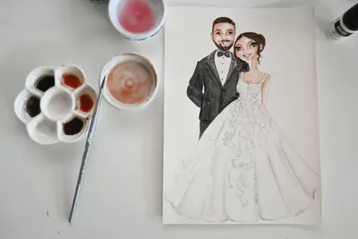 Watercolour bride and groom illustration beside a paint palette, brush and water jar, by Lisa Catanea