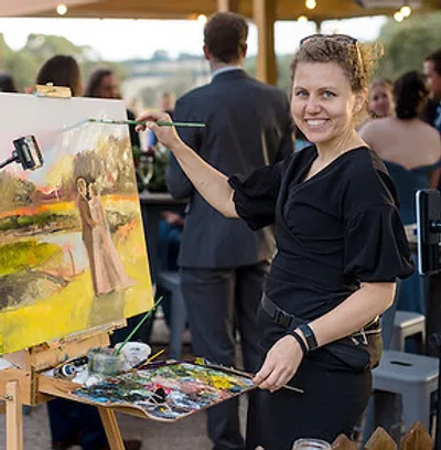 Olga painting a wedding couple live at her easel during an outdoor reception by Wedding Day Painter