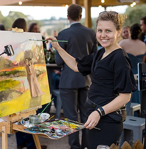 Olga painting a wedding couple live at her easel during an outdoor reception by Wedding Day Painter